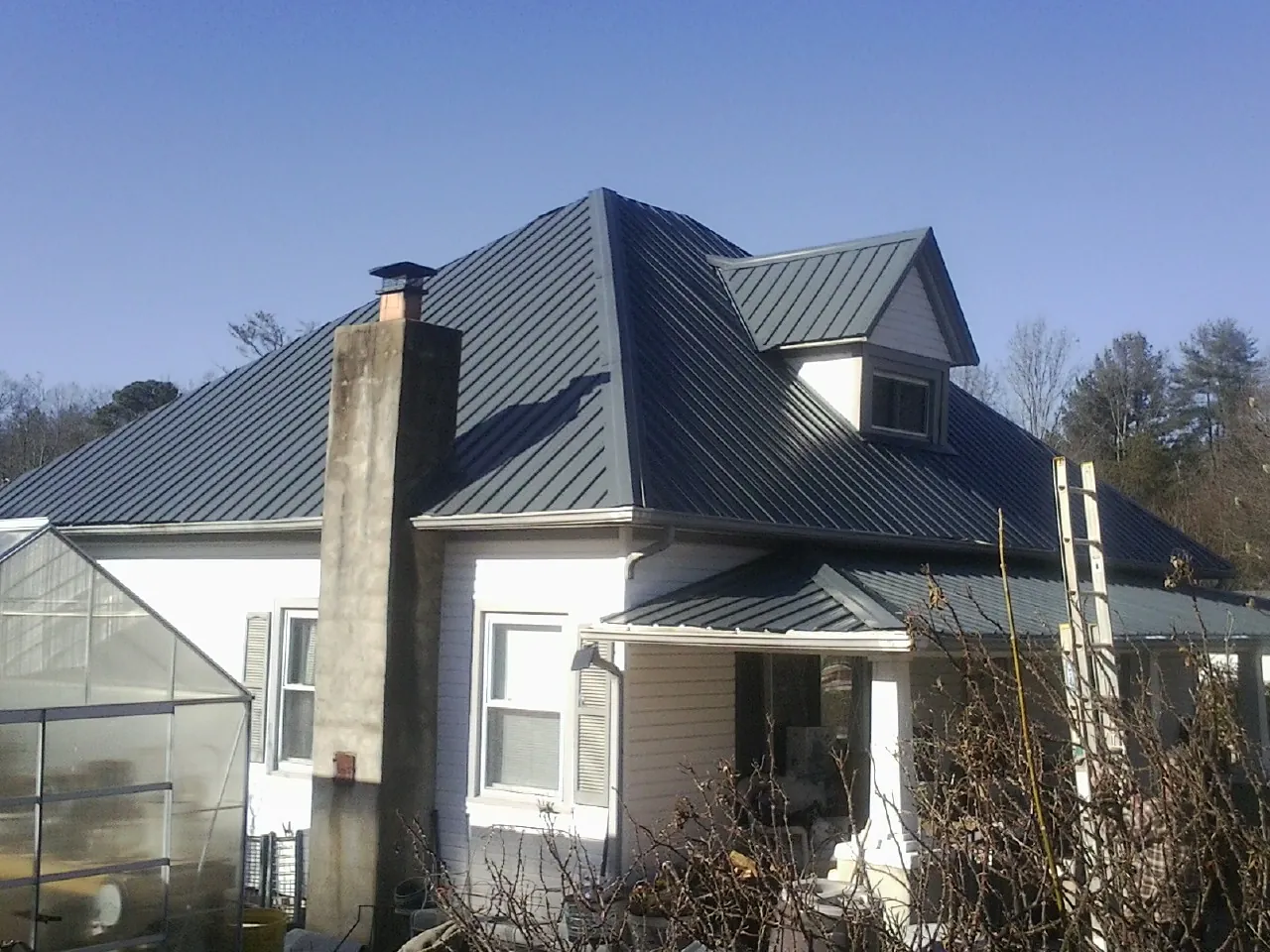 Dark blue standing seam metal roof on a white farmhouse with dormer — Slate & Tile Roof Repair by Roofing Brothers in Grifton