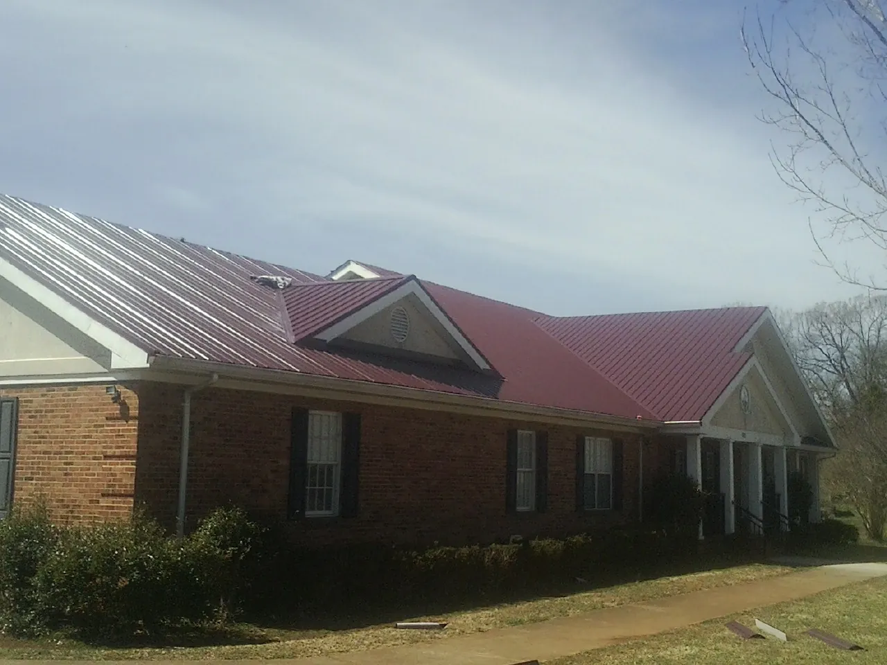 Red metal roof with gabled entries on a long brick building, from a Hail Damage Roof Repair job in Grifton