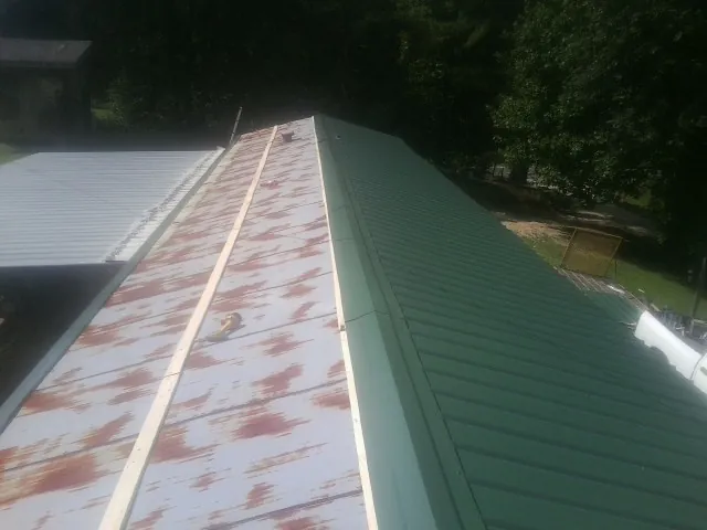 Old rusted panels beside newly installed green metal roofing — Wind Damage Roof Repair by Roofing Brothers in Grifton