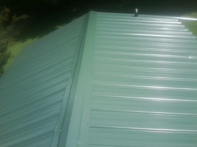 New green metal panels meeting at the ridge of a roof — Flat Roof Repair work by our crew in Grifton