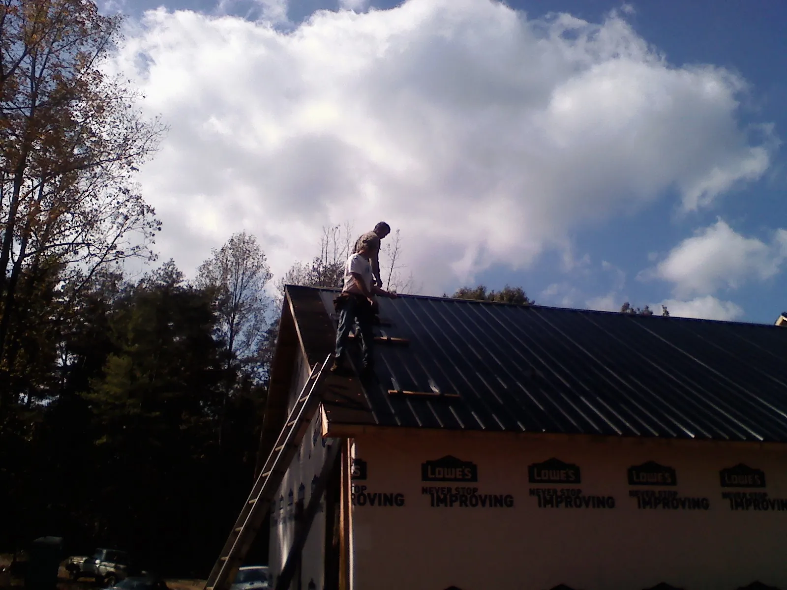 Roofer fastening dark metal panels high against a cloudy sky, from a Roof Inspection job in Grifton