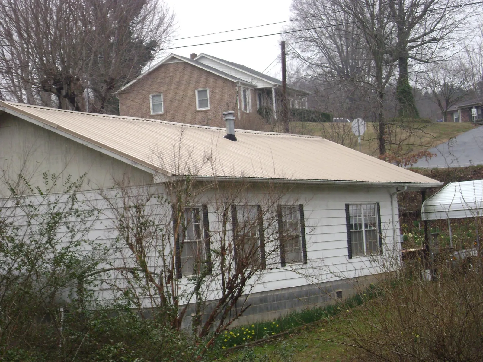 Tan metal roof on a white sided house set into a hillside — Commercial Roofing by Roofing Brothers in Grifton