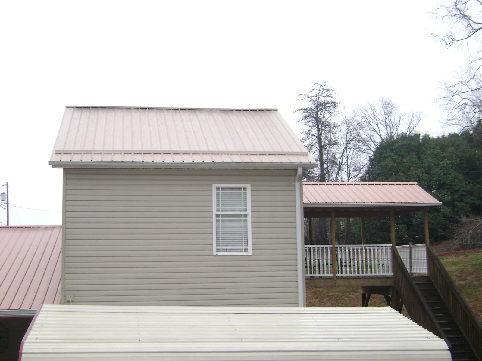 Tan metal roofs on a two story addition and attached porch, from a Roof Replacement job in Grifton